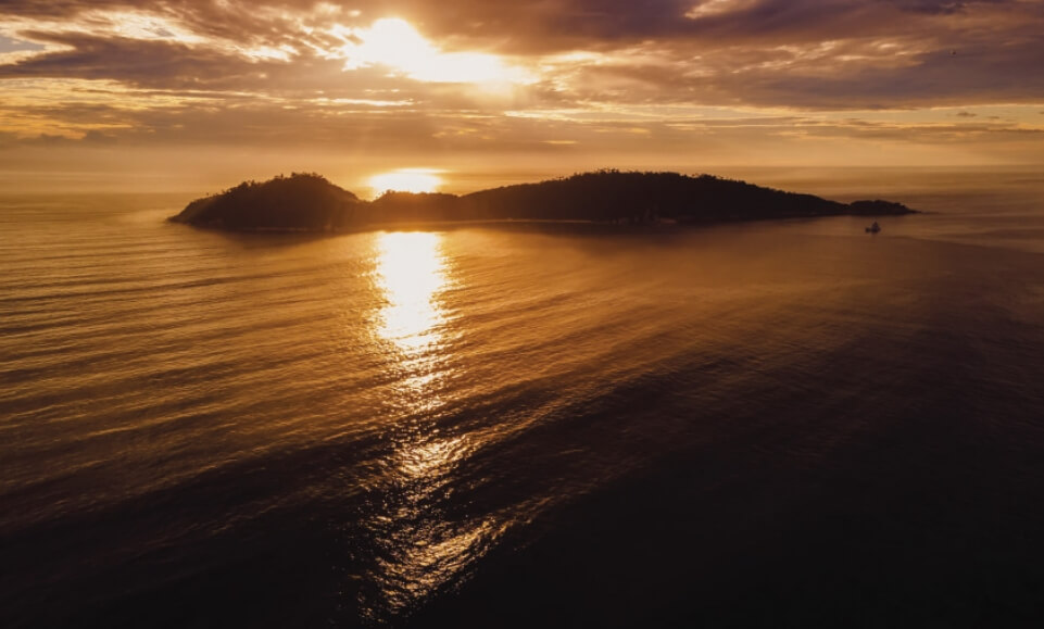 Foto aérea de um nascer do sol em Florianópolis, no centro da foto encontra-se a ilha do Campeche